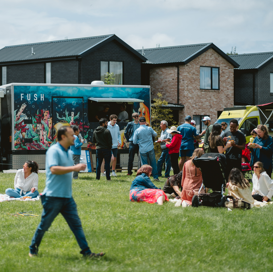 Home Capital Partners – community gathering on a grassy reserve beside a food truck, with people and new townhouses in the background.