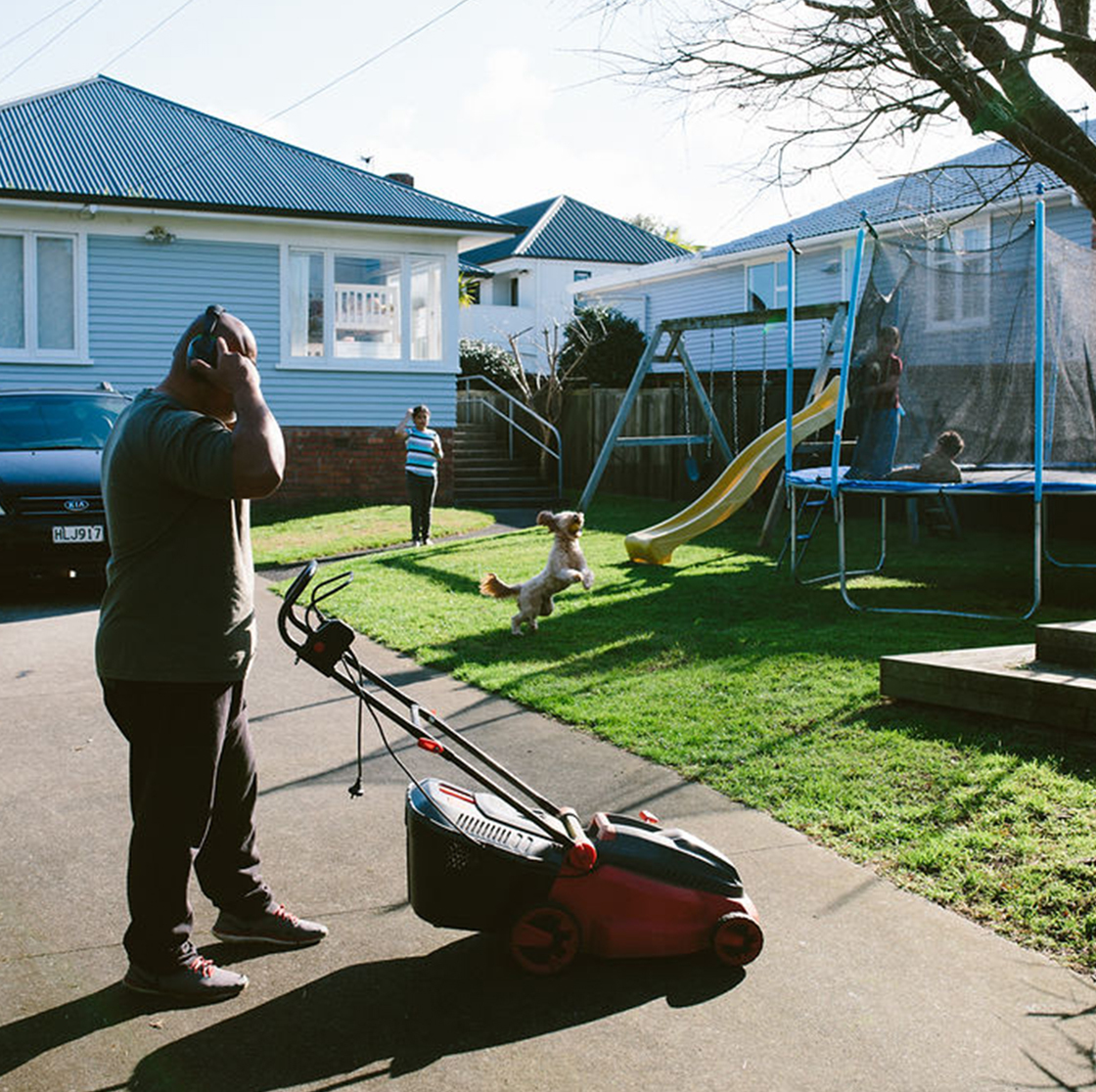 Home Capital Partners – person mowing a backyard while a dog jumps and children play on a trampoline and slide.