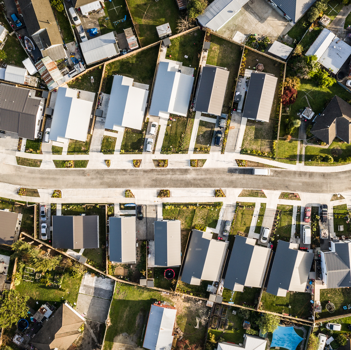 Home Capital Partners – aerial view of a neighbourhood street lined with modern single-storey homes, driveways and fenced backyards.