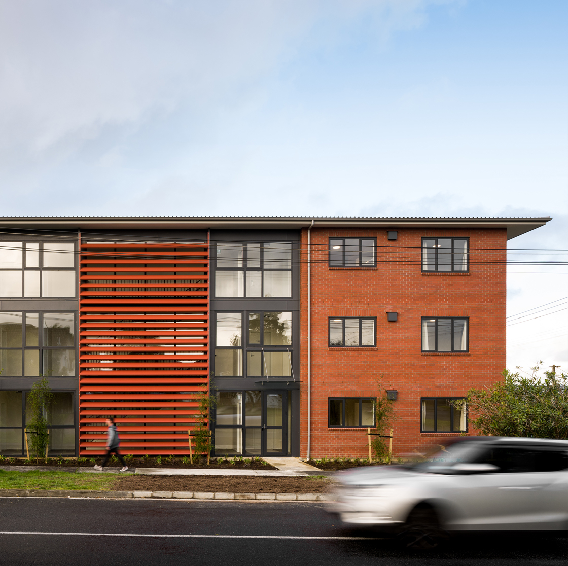 Home Capital Partners – street view of a three-storey brick apartment building with orange louvered panels; a person walking and a car passing in front.