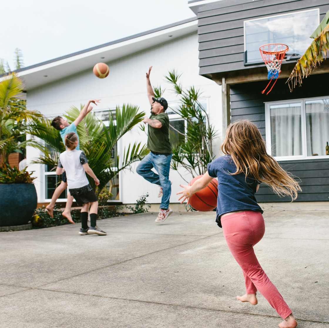 Home Capital Partners – children and an adult playing basketball in a home driveway outside a modern house.