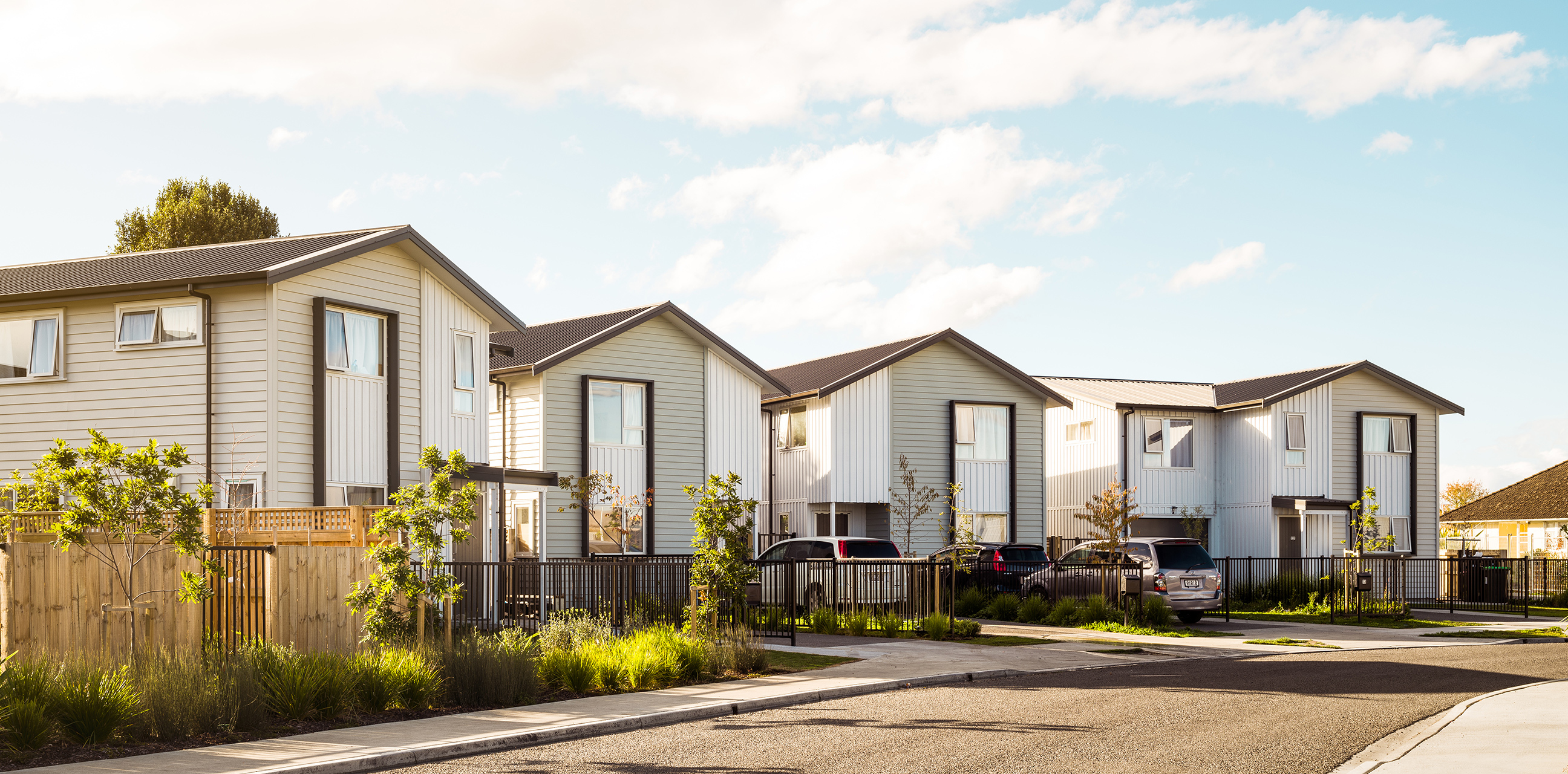 Home Capital Partners – street view of modern two-storey townhouses with fences, young trees and parked cars along a quiet residential street.