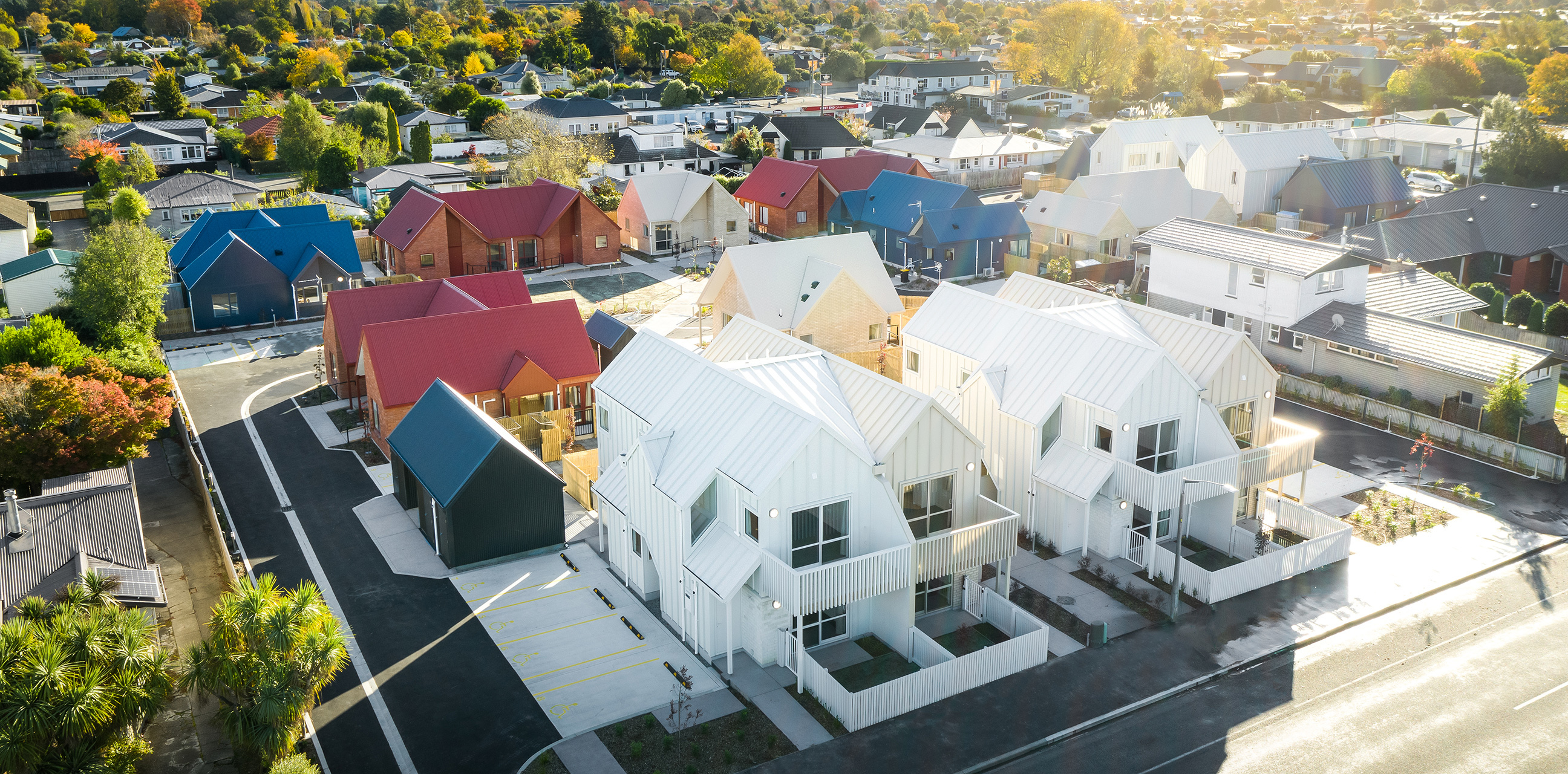 Home Capital Partners – aerial view of a new housing development: white gabled townhouses with fenced courtyards and marked parking in a suburban neighborhood on High Street in Rangiora, North Canterbury.