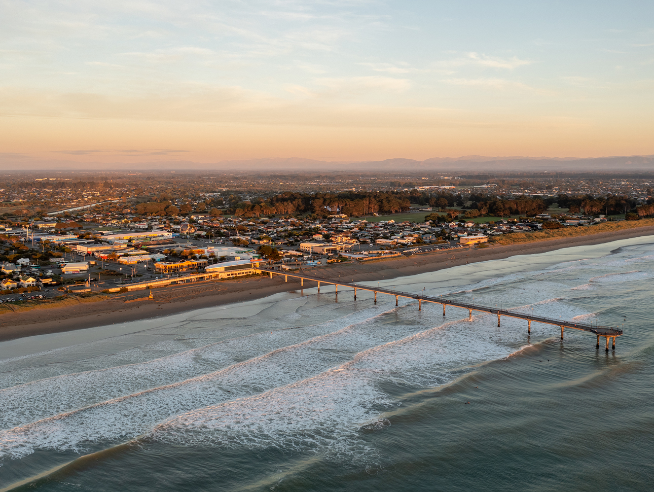 Home Capital Partners – aerial view of a beachside suburb of New Brighton Christchurch, with a long pier and surf.