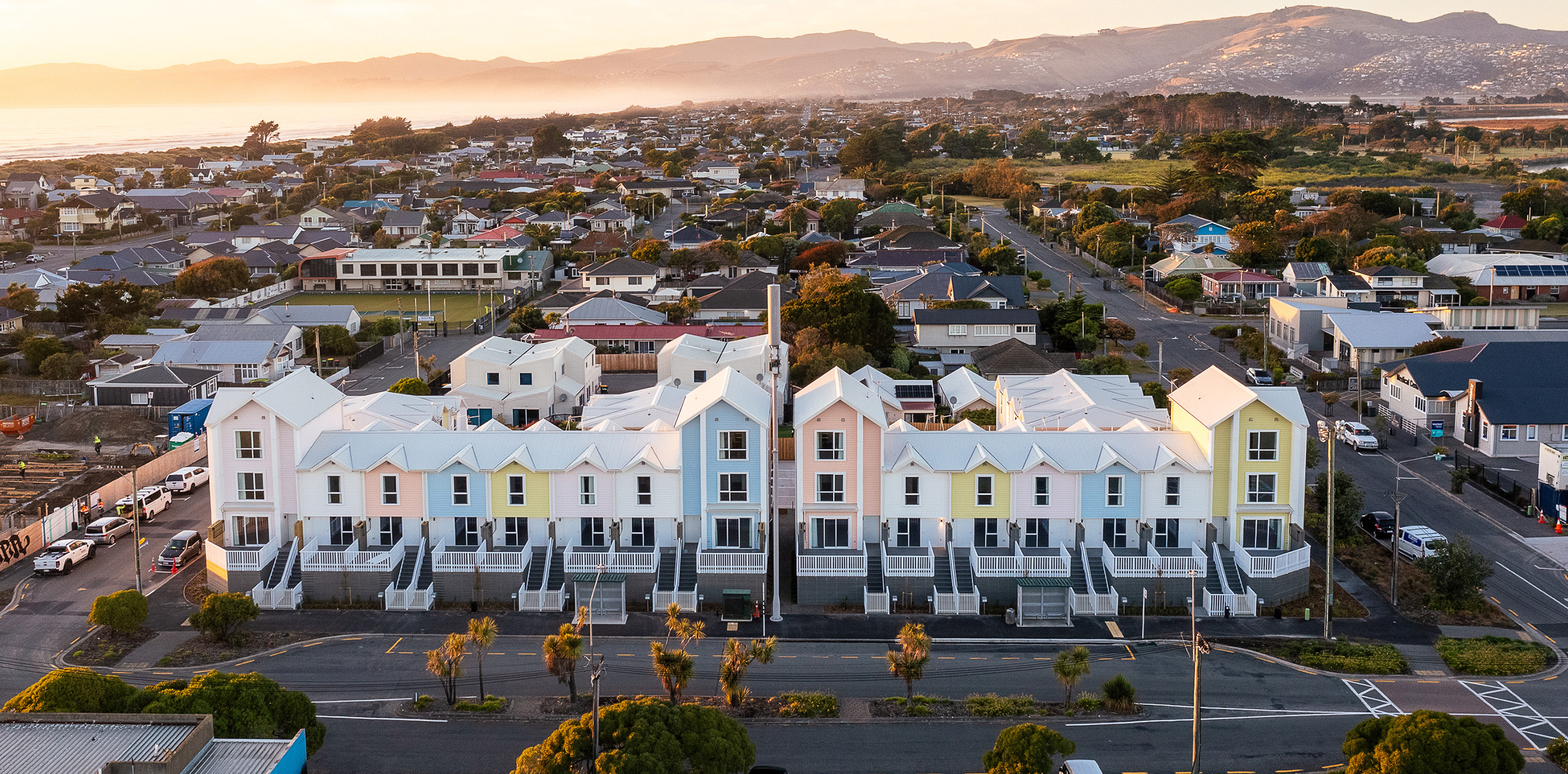 Home Capital Partners – aerial view of the Te Pākau Maru development in New Brighton, Christchurch, with a row of pastel-colored terraced homes near the coastline.