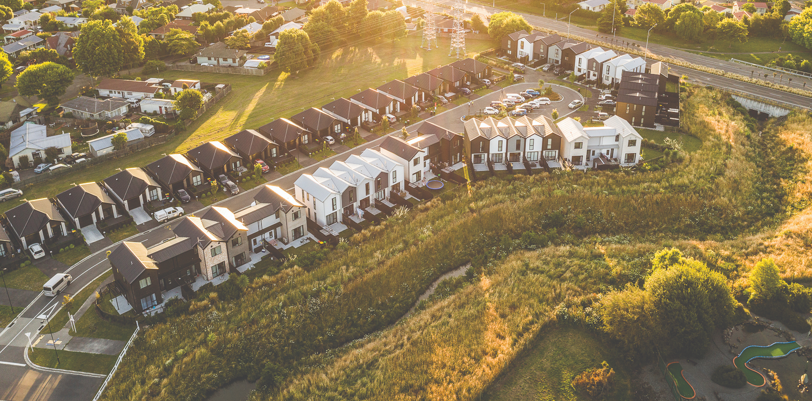 Home Capital Partners – aerial view of a modern townhouse neighbourhood beside a grassy reserve and roadway. The Residences of Karamū, located in Broomfield, Christchurch.